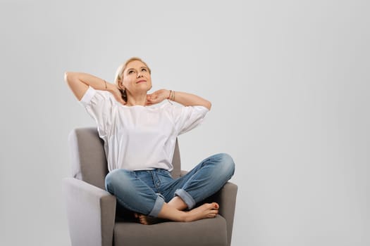 Senior woman relaxing in an armchair crossing legs and hold hands behind her head