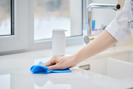 Female hand with washing sponge cleaning stone surface of kitchen tabletop (photo with shallow depth of field)