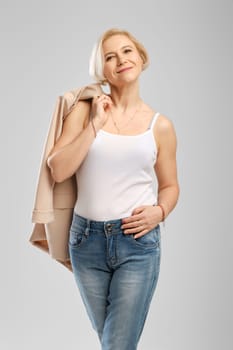 Studio portrait of successful middle age woman, self-confident holding beige jacket over the shoulder in studio