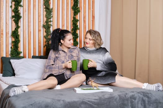 Elder mother and daughter sitting on bed, share impressions, talking