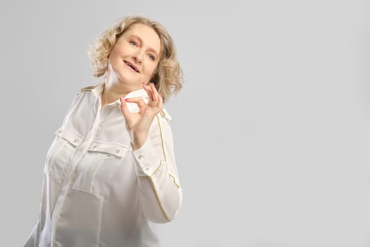 Happy senior woman shows ok gesture over grey studio background, photo with place for text