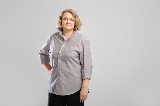 Casual portrait of senior woman in grey shirt and trousers over grey studio background