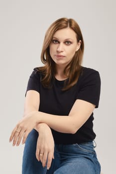 Portrait of young woman in black t shirt and jeans posing over grey background