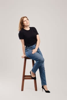 Young woman in black t shirt and jeans thinking and looking up over grey background