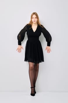 Tense young woman pushes off with her hands from grey wall, leaned forward