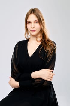 Studio portrait of calm and positive young woman with crossed arms over grey background