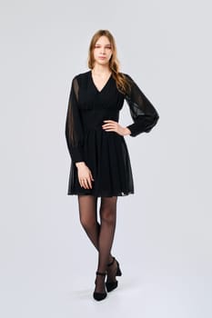 Young woman posing in studio in little black dress with one arm on waist