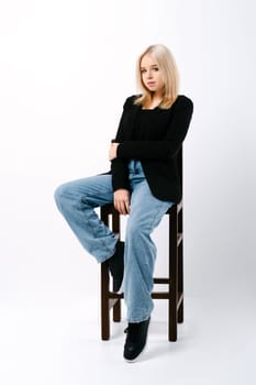 girl in tank top, jacket and jeans sits on chair in studio