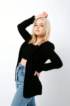 Blonde girl in tank top, jacket and jeans posing as a fashion model over grey background