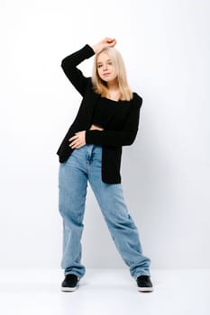 Blonde teenager girl in tank top, jacket and jeans posing as a fashion model over grey background