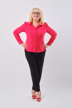 Stylish positive middle aged female with curly blonde hair standing with hands on waist over grey background