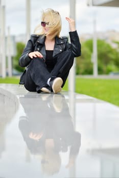 Girl in black clothes sits on railing in windy day