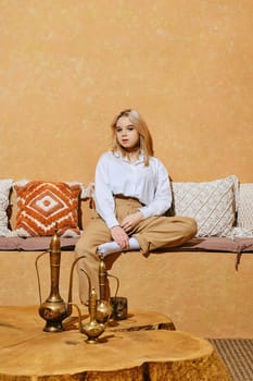 Funny girl sitting cross-legged in comfortable Middle Eastern style room