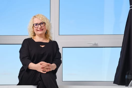 Happy senior woman in glasses sits on windowsill