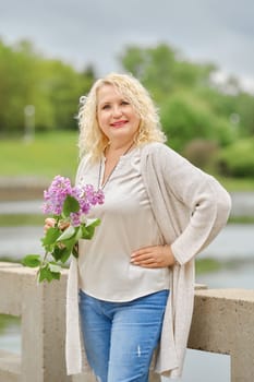Cheerful senior woman walks along the embankment with a branch of lilac in her hands