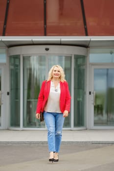 Satisfied senior woman walks out the bank or office building, she is full of hopes and expectations