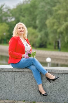 Happy middle-aged woman sits on the embankment in a city park