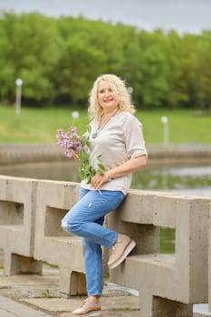 Smiling senior woman walks along the embankment with a branch of lilac in her hands