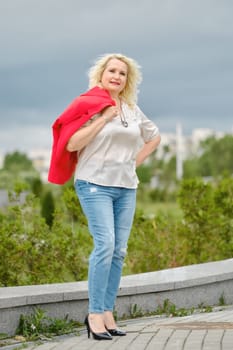 Cheerful senior woman walks in the city, she slung her jacket over her shoulder