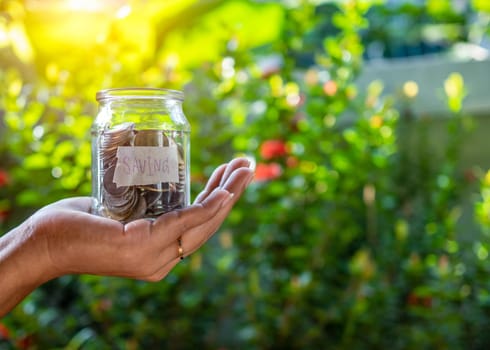 Hand human and Piggy bank bottle with saving sign on natural bokeh background.