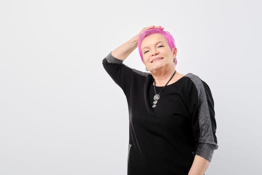 Happy old woman runs her hand through her short pink hair over white background