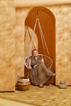 Old active woman with pink hair sits in wicker swing in arch