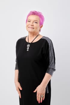 Happy old woman with short pink hair runs her hand through her knitted dress over white background