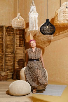 Cheerful and careless old woman with pink hair sitting on wicker padded stool