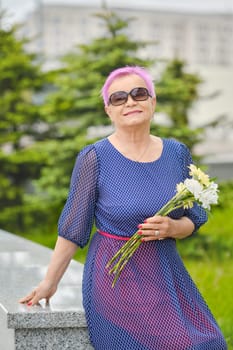 Portrait of smiling mature woman with short pink hair standing near fir-tree on the street