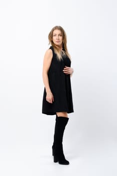 Full length portrait of stylish and fashionable senior woman in loose black dress and suede boots over white studio background
