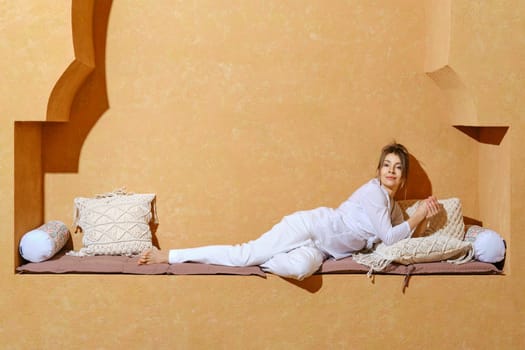 Stylish middle aged female pensioner wearing white shirt and trousers relax on oriental style wall bench