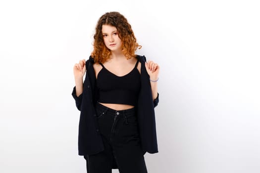 Serene caucasian teenage girl in casual clothing with colored ends of hair holds edges of black shirt over white studio background
