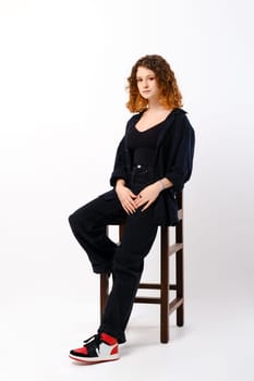 Young girl sitting on tall chair in studio over white background