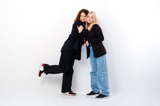 Two teen girls lean on each other over white studio background