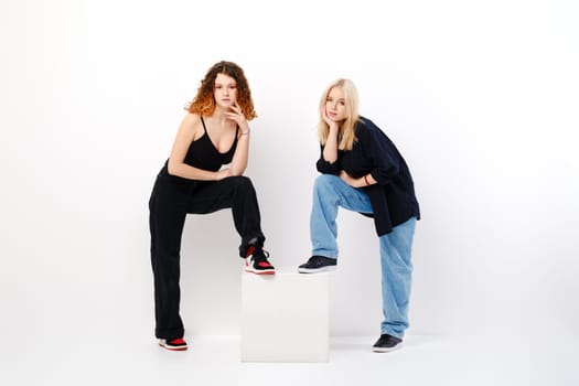 Two teen girls lean on square box over white studio background