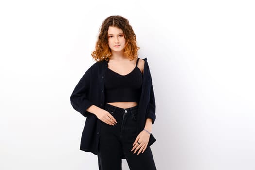 Calm european teenage girl in casual clothing with colored ends of hair wearing black tank top and shirt over white studio background