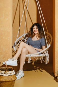 Cute young girl seated in a wicker swing in harsh light
