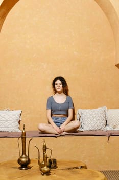 Funny girl sitting cross-legged in comfortable Middle Eastern style room