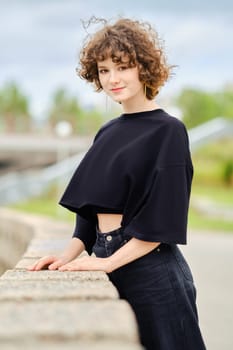 Teenager girl in black clothes leaning on stone parapet in city park