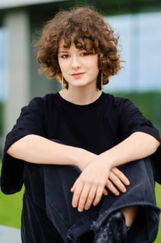 Portrait of cute teenager girl in wide black jeans, shirt and rough boots outdoors