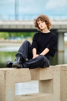 Portrait of smiling teenager girl in black jeans, t-shirt and rough boots near the river