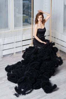 Gorgeous woman in a luxurious puffy black dress sits on a swing