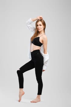 Full length studio portrait of young barefoot woman in black jean and shirt in profile