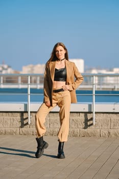 Street fashion, women casual and trendy outfit. Woman in pantsuit, leather tank-top and rough boots outdoor.