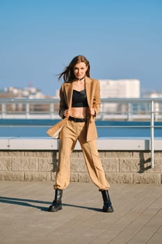 Street fashion, women casual and trendy outfit. Woman in pantsuit, leather tank-top and rough boots outdoor.