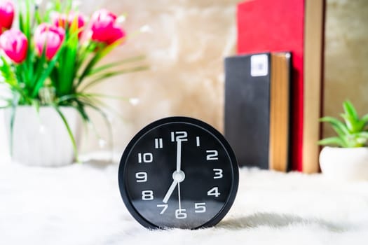 Black alarm clock and book with pink flower on table