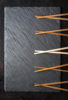 Black sushi slate board with wooden chopsticks with copyspace. Top view. Asian food background.
