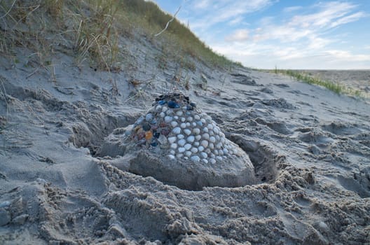 Sand castle with shells and sand. Moat around the castle in front of dunes. On the beach in Denmark by the sea. Landscape photo