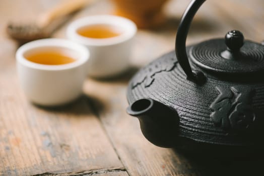 Still life with traditional asian herbal tea prepared in vintage cast iron teapot with organic dry herbs on rustic wooden table.