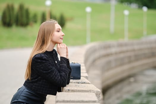 Cute woman leans against the railing and looks thoughtfully at the river